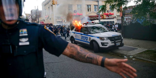 New York Police officers push back protesters as a police car burns during a demonstration, Saturday, May 30, 2020, in the Brooklyn borough of New York. (AP Photo/Seth Wenig)