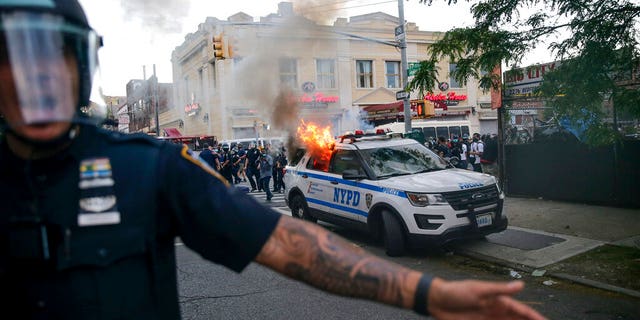 New York Police officers push back protesters as a police car burns during a demonstration, Saturday, May 30, 2020, in the Brooklyn borough of New York. (AP Photo/Seth Wenig)