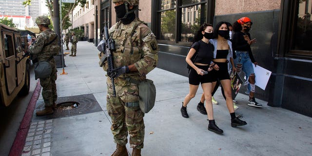 People walk by as a member of the California National Guard stands watch Sunday, May 31, 2020, in Los Angeles.