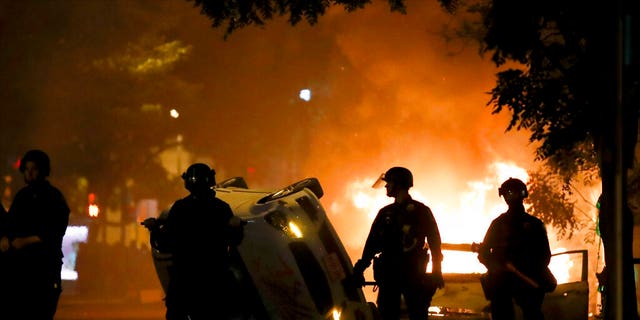 Police stand near a overturned vehicle and a fire as demonstrators protest the death of George Floyd, Sunday, May 31, 2020, near the White House in Washington. Floyd died after being restrained by Minneapolis police officers (AP Photo/Alex Brandon)