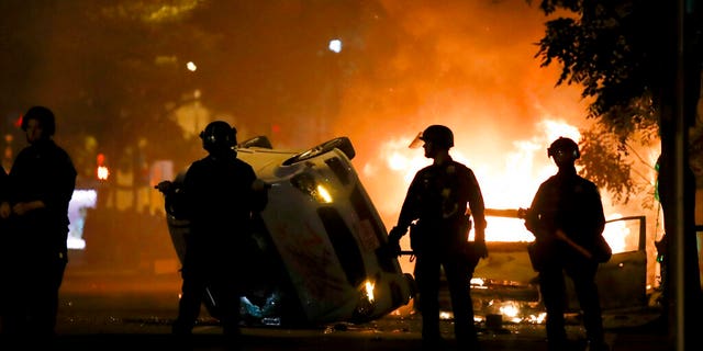 Police stand near a overturned vehicle and a fire as demonstrators protest the death of George Floyd, Sunday, May 31, 2020, near the White House in Washington. Floyd died after being restrained by Minneapolis police officers (AP Photo/Alex Brandon)