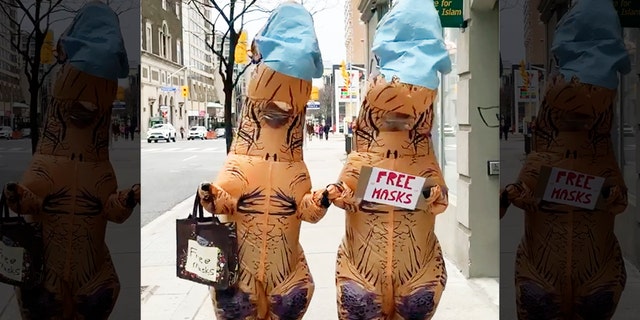 In videos of the dinosaur duo, the pair are holding up signs advertising “free masks” and holding out bags for people to help themselves.