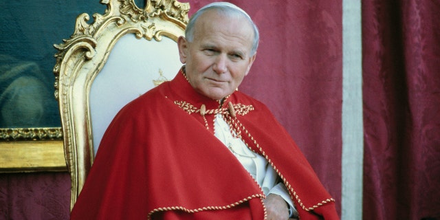 (File photo from 1982) Close-up of Pope John Paul II sitting on a chair, wearing red robes with a portrait of the St. Theresa of Avila in the background during his visit to Avila, Spain.