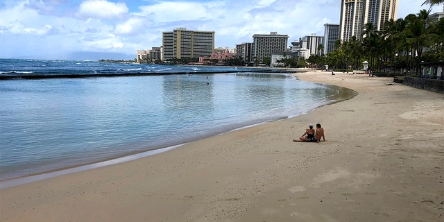 March 28, 2020: A couple sits on an empty section of Waikiki Beach in Honolulu. Hawaii law enforcement authorities are cracking down on rogue tourists who are visiting beaches, jetskiing, shopping and generally flouting strict requirements that they quarantine for 14 days after arriving.