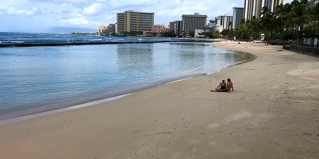 March 28, 2020: A couple sits on an empty section of Waikiki Beach in Honolulu. Hawaii law enforcement authorities are cracking down on rogue tourists who are visiting beaches, jetskiing, shopping and generally flouting strict requirements that they quarantine for 14 days after arriving.