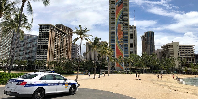 A police officer arrives to tell people to leave Waikiki Beach in Honolulu. Hawaii law enforcement authorities are cracking down on rogue tourists who are visiting beaches, jetskiing, shopping and generally flouting strict requirements that they quarantine for 14 days after arriving. (AP Photo/Caleb Jones, File)