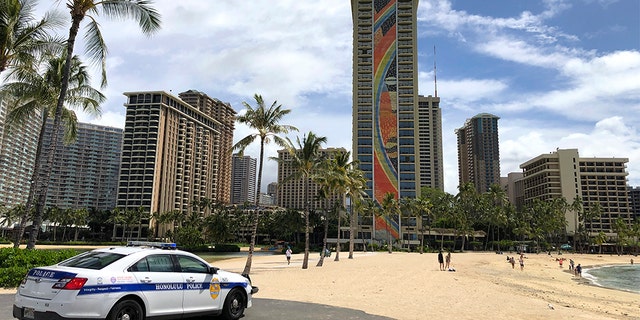 A police officer arrives to tell people to leave Waikiki Beach in Honolulu. Hawaii law enforcement authorities are cracking down on rogue tourists who are visiting beaches, jetskiing, shopping and generally flouting strict requirements that they quarantine for 14 days after arriving. (AP Photo/Caleb Jones, File)