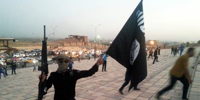 A fighter holding an ISIS flag and a weapon on a street on June 23, 2014.