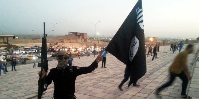 A fighter holding an ISIS flag and a weapon on a street on June 23, 2014.