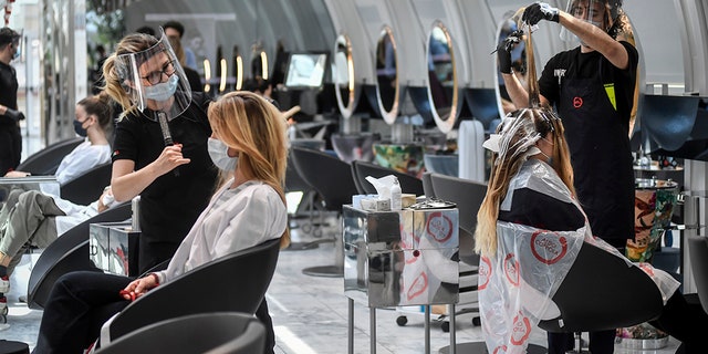 Los clientes se arreglan el cabello en una peluquería en Milán, Italia, el lunes 18 de mayo de 2020, ya que Italia está levantando lentamente las restricciones sanitarias después de un bloqueo de coronavirus de dos meses.  (Claudio Furlan / LaPresse a través de AP)