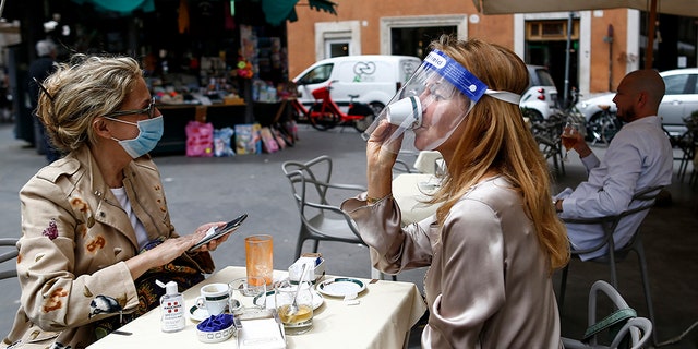 A woman sips her coffee from under her facial protection at a cafe with outdoor tables in Rome Monday, May 18, 2020. Italy is slowly lifting restrictions after a two-month coronavirus lockdown. (Cecilia Fabiano /LaPresse via AP)