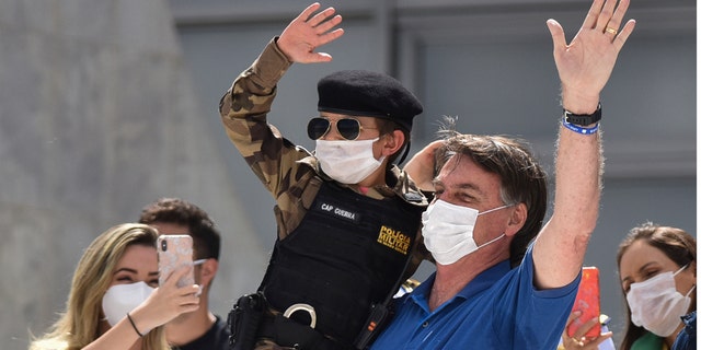 Brazil's President Jair Bolsonaro, wearing a mask against the spread of the new coronavirus, carries a child dressed in military policeman's uniform during a protest against the Supreme Court and Brazil's National Congress, to back his open-the-economy drive amid the pandemic, in Brasilia, Brazil, Sunday, May 17, 2020. Bolsonaro greeted hundreds of supporters who gathered at the presidential residence to back his open-the-economy drive even as the COVID-19 pandemic sweeps across the country. (AP Photo/Andre Borges)