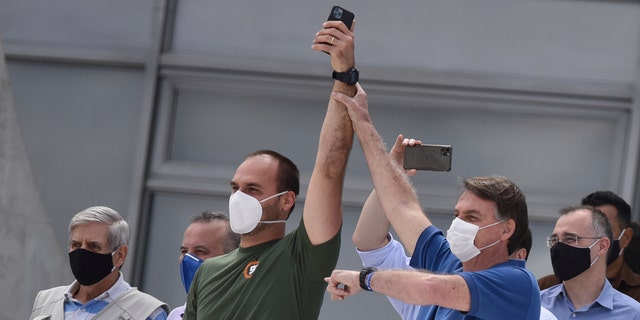 Brazil's President Jair Bolsonaro, right, wearing a mask against the spread of the new coronavirus, raises the arm of his son Eduardo Bolsonaro during a protest against the Supreme Court and Brazil's National Congress, and to back his open-the-economy drive amid the pandemic, in Brasilia, Brazil, Sunday, May 17, 2020. Bolsonaro greeted hundreds of supporters who gathered at the presidential residence to back his open-the-economy drive even as the COVID-19 pandemic sweeps across the country. (AP Photo/Andre Borges)