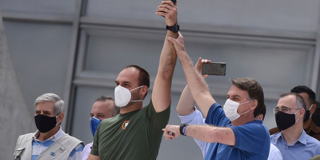 Brazil's President Jair Bolsonaro, right, wearing a mask against the spread of the new coronavirus, raises the arm of his son Eduardo Bolsonaro during a protest against the Supreme Court and Brazil's National Congress, and to back his open-the-economy drive amid the pandemic, in Brasilia, Brazil, Sunday, May 17, 2020. Bolsonaro greeted hundreds of supporters who gathered at the presidential residence to back his open-the-economy drive even as the COVID-19 pandemic sweeps across the country. (AP Photo/Andre Borges)