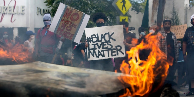 People hold signs and shout behind a burning police vehicle in Los Angeles, Saturday, May 30, 2020, during a protest over the death of George Floyd. (Associated Press)