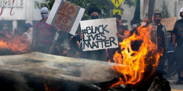 People hold signs and shout behind a burning police vehicle in Los Angeles, Saturday, May 30, 2020, during a protest over the death of George Floyd. (Associated Press)