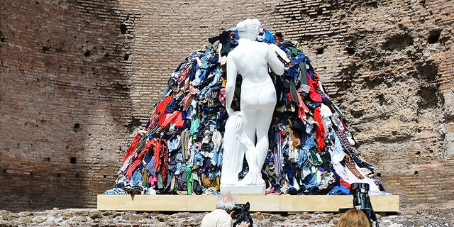 People stand in front of rags, polystyrene and acrylic cement coating sculpture " Venere degli stracci " made by Italian artist Michelangelo Pistoletto during the opening of the " Post Classici " exhibition at Rome's ancient Forum. (VINCENZO PINTO/AFP via Getty Images)