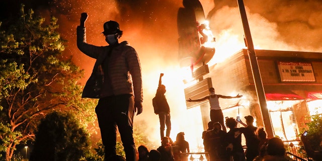 Protestors demonstrate outside of a burning fast food restaurant, Friday, May 29, 2020, in Minneapolis. Protests over the death of George Floyd, a black man who died in police custody Monday, broke out in Minneapolis for a third straight night. (AP Photo/John Minchillo)