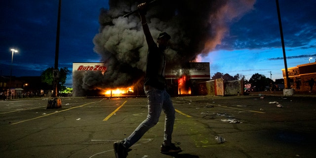 A man poses in the parking lot of an AutoZone store in flames, while protesters hold a rally against the death of George Floyd in Minneapolis on May 27. (Carlos Gonzalez/Star Tribune via AP)