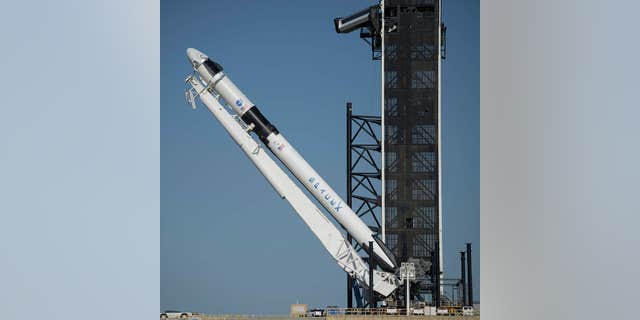 The SpaceX Falcon 9 rocket with the company's Crew Dragon spacecraft onboard is visible as it is elevated to a vertical launch pad position at the Launch Complex 39A.