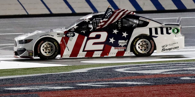 Brad Keselowski holds an American flag after winning the NASCAR Cup Series auto race at Charlotte Motor Speedway early Monday, May 25, 2020, in Concord, N.C. (AP Photo/Gerry Broome)