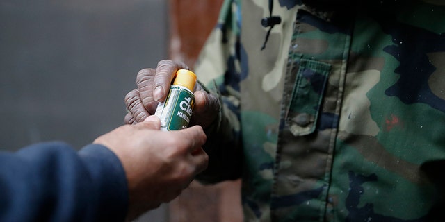 In this Friday, April 24, 2020, photo, Juan De La Cruz, left, hands a bottle of hand sanitizer to a visitor who collected a bag of donated food through the Coalition for the Homeless organization at St. Bartholomew's Episcopal Church in New York. (AP Photo/John Minchillo)