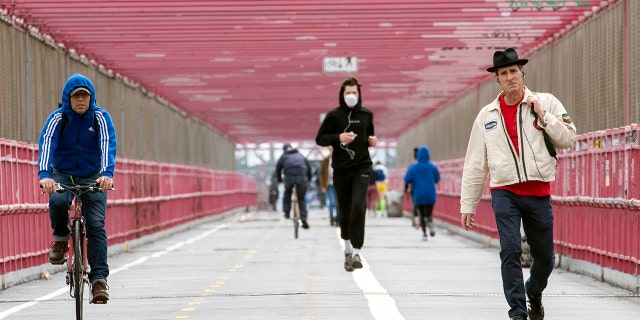 In this Monday, May 11, 2020 photo, a jogger wearing a face masks runs in between a biker and a pedestrian not wearing masks as they make their way over the Williamsburg bridge in New York.New York's governor has ordered masks for anyone out in public who can't stay at least six feet away from other people. Yet, while the rule is clear, New Yorkers have adopted their own interpretation of exactly when masks are required, especially outdoors. (AP Photo/Mary Altaffer)