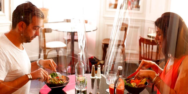 A man and a woman demonstrate dining under a Plex'Eat plastic shield Wednesday, May 27, at Paris restaurant H.A.N.D.