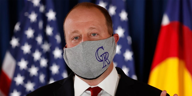 Colorado Governor Jared Polis makes a point while wearing a face mask with the logo of Major League Baseball's Colorado Rockies during a news conference to update the state's efforts to control the spread of the new coronavirus Friday, May 15, 2020, in the State Capitol in Denver.