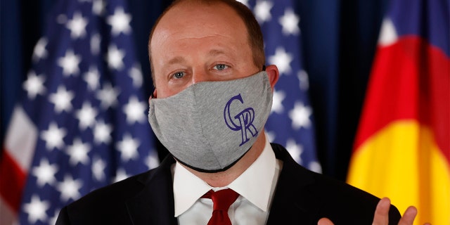 Colorado Governor Jared Polis makes a point while wearing a face mask with the logo of Major League Baseball's Colorado Rockies during a news conference to update the state's efforts to control the spread of the new coronavirus Friday, May 15, 2020, in the State Capitol in Denver.