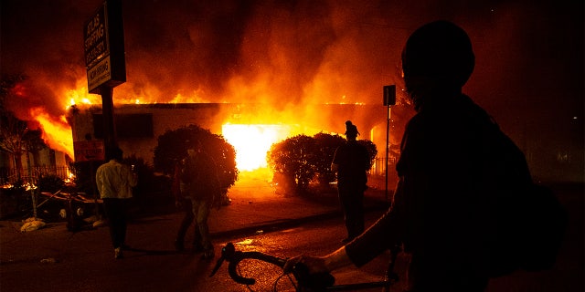 A protester looks on at a burning building in Minneapolis, early Saturday, May 30, 2020, amid protests against the death of George Floyd in police custody on Memorial Day. (Khadejeh Nikouyeh/News & Record via AP)