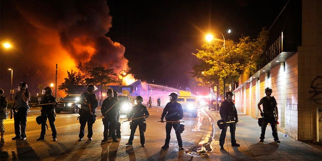 Police stand watch as a firefighters put out a blaze Saturday, May 30, 2020, in Minneapolis. AP Photo/Julio Cortez