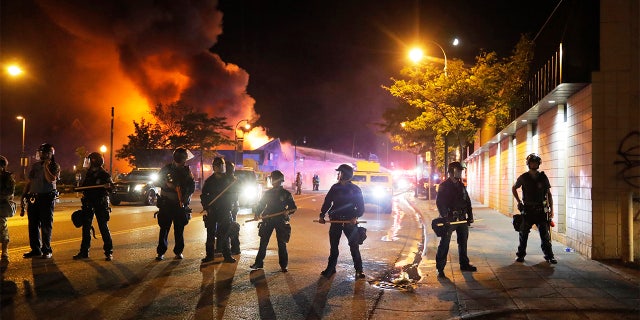 Police stand watch as a firefighters put out a blaze Saturday, May 30, 2020, in Minneapolis. AP Photo/Julio Cortez