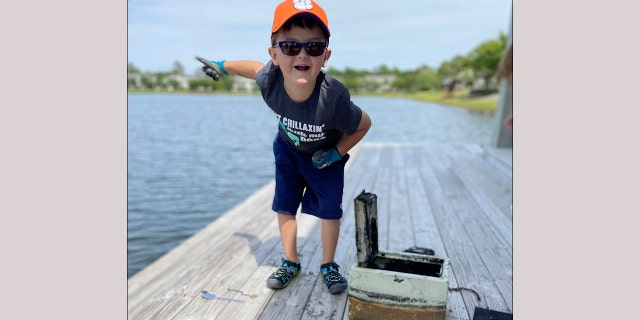 In this May 9, 2020, photo provided by Catherine Brewer, Knox Brewer stands next to a safe he pulled out of Whitney Lake in South Carolina. The 6-year-old was using a magnet attached to a string to fish for metal in the water when he reeled in a lockbox that police said was stolen from a woman who lived nearby eight years ago. (Catherine Brewer via AP)