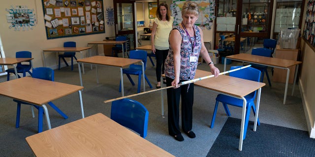 Year 6 teacher Jane Cooper uses a 2 meter length of ruler and pipe to check seat spacings in her classroom as measures are taken to prevent the transmission of coronavirus before the possible reopening of Lostock Hall Primary school in Poynton near Manchester, England, Wednesday May 20, 2020. (AP Photo/Jon Super)