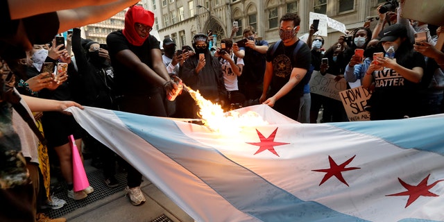 A person burns a Chicago flag during a protest over the death of George Floyd in Chicago, Saturday, May 30, 2020.