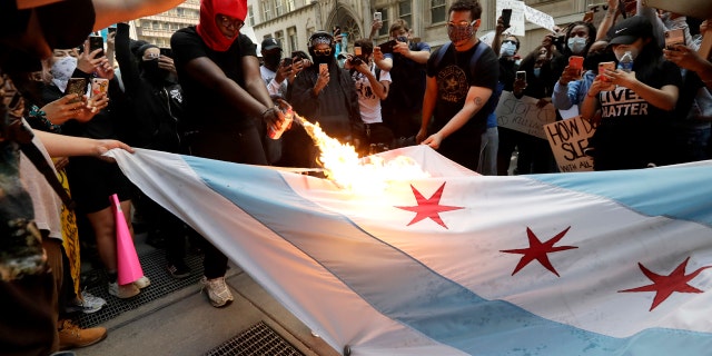 A person burns a Chicago flag during a protest over the death of George Floyd in Chicago, Saturday, May 30, 2020.