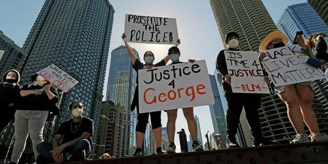 People hold signs during a protest over the death of George Floyd in Chicago, Saturday, May 30, 2020.