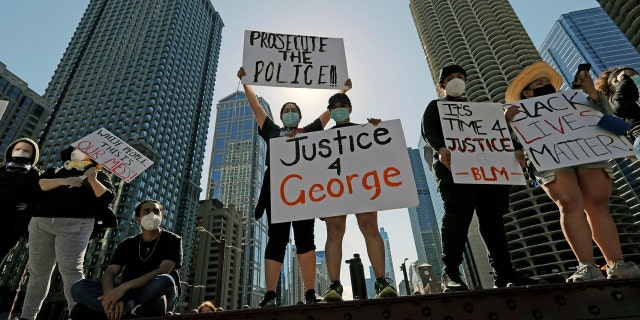 People hold signs during a protest over the death of George Floyd in Chicago, Saturday, May 30, 2020.