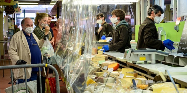 Customers, wearing protective facemasks, queue at the cheese counter in order to be served behind a transparent plastic curtain at a covered market in Le Perreux-sur-Marne on April 19. (BERTRAND GUAY/AFP via Getty Images)