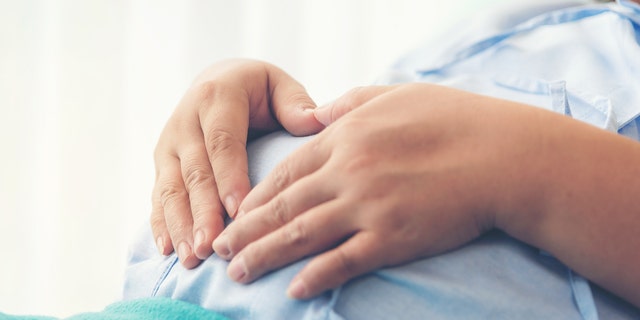 Pregnant woman holds belly from hospital bed