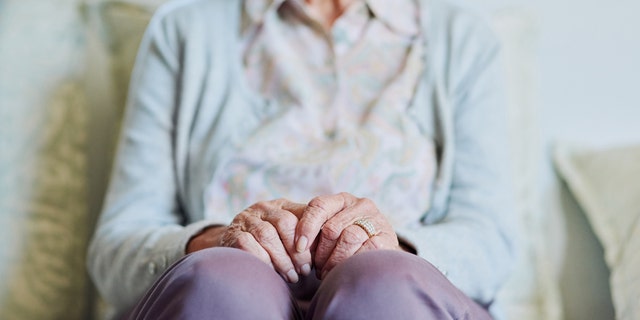 A senior woman sits on the sofa alone in the living room of a nursing home. For some people, the aging process moves more quickly than for others, which is referred to as 