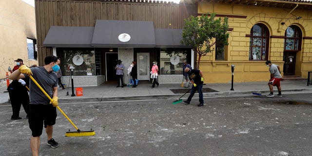 People helping clean up broken glass and debris after the riots over the death of George Floyd, Sunday in La Mesa, Calif. (AP Photo/Gregory Bull)