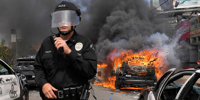 Los Angeles Police Department commander Cory Palka stands among several destroyed police cars as one explodes while on fire during a protest over the death of George Floyd, Saturday, May 30, 2020, in Los Angeles.