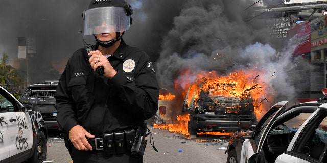 Los Angeles Police Department commander Cory Palka stands among several destroyed police cars as one explodes while on fire during a protest over the death of George Floyd, Saturday, May 30, 2020, in Los Angeles.