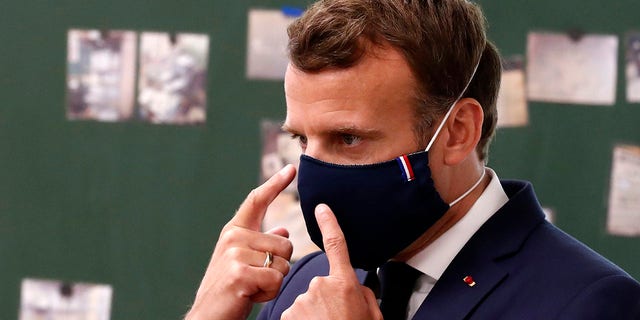 Macron wears a protective face mask with a blue-white-red colored ribbon as he speaks with schoolchildren during a class Tuesday while visiting the Pierre Ronsard elementary school in Poissy, outside Paris. (Ian Langsdon, Pool via AP)