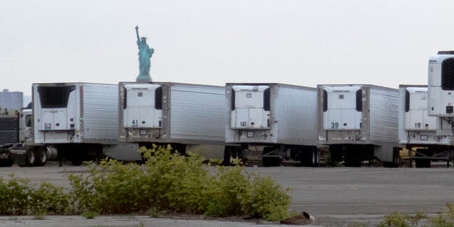 The Statue of Liberty rises in the distance above refrigerated trucks intended for storing corpses that are staged in a lot at the 39th Street pier in Brooklyn. (AP)