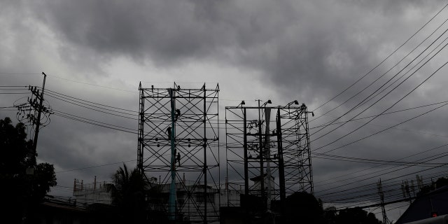 Dark clouds envelop the skies as workers fold a billboard to prepare for the coming of typhoon Vongfong in Manila, Philippines Thursday May, 14, 2020.