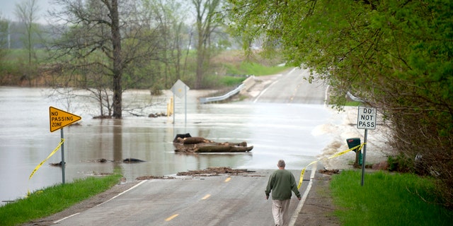 Freeland resident Cyndi Ballien walks up to get a closer look as heavy rain floods North Gleaner Road near its intersection with Tittabawassee Road on Tuesday, May 19, 2020, in Saginaw County, Mich.