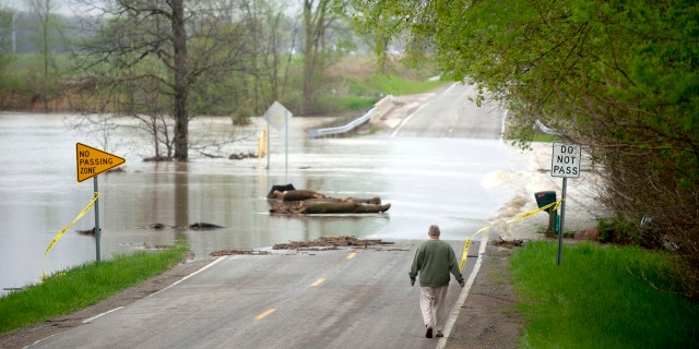 Freeland resident Cyndi Ballien walks up to get a closer look as heavy rain floods North Gleaner Road near its intersection with Tittabawassee Road on Tuesday, May 19, 2020, in Saginaw County, Mich.